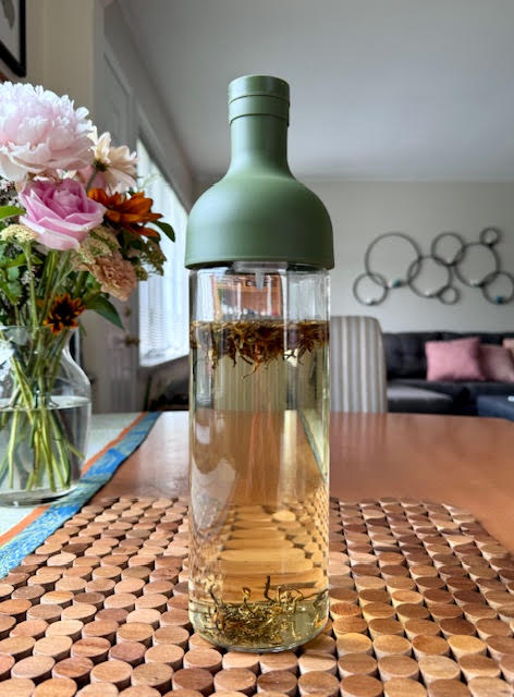 Hario Cold Brew Tea Wine Bottle with green top holding loose leaf black tea ready to steep. A  bouquet of flowers is nearby.