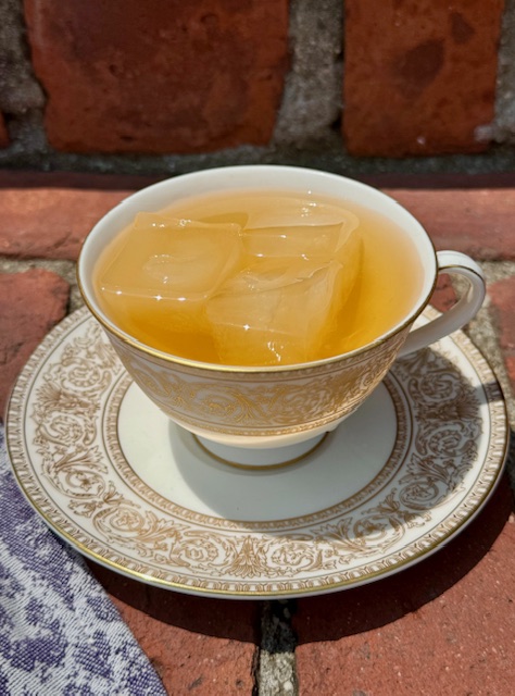 Iced tea in a white teacup with a gold filagree pattern and a matching saucer beneath it.