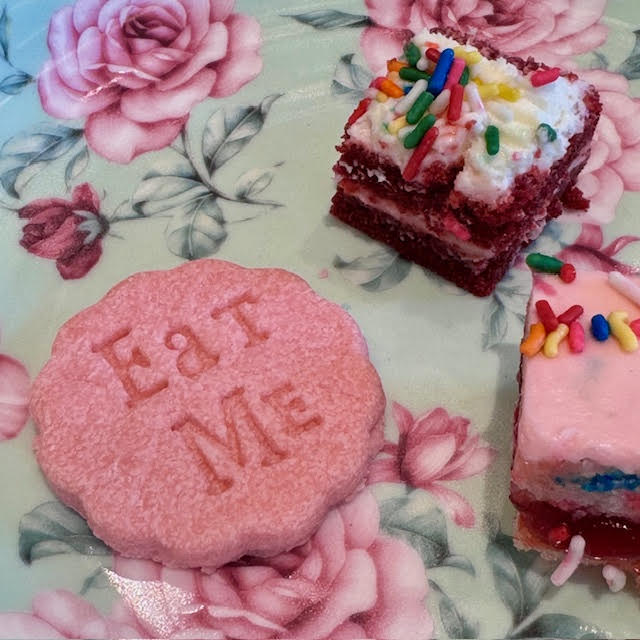 "Eat Me," Alice-in-Wonderland-inspired pink cookie at the NYBG Wonderland afternoon tea. Little cake squares are nearby on a floral dessert plate.