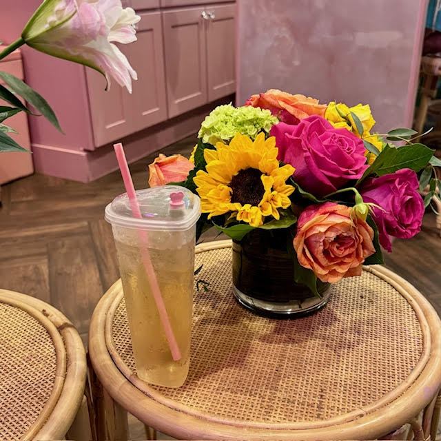 Iced tea in a heart-shaped clear cup with a pink straw next to a colorful bouquet at BesTea.