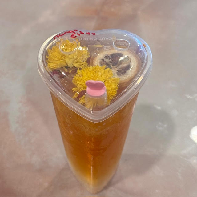 Heart-shaped cup of iced tea with edible flowers and a pink beverage plug at BesTea in Babylon, NY.