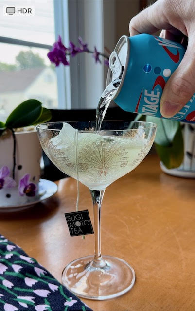 Pouring seltzer over a Yuzu Matcha Sencha teabag into a tall coupe glass