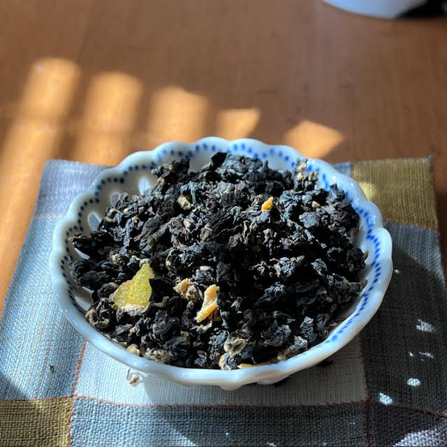 Partly rolled black tea leaves with pieces of dried bergamot in a white dish