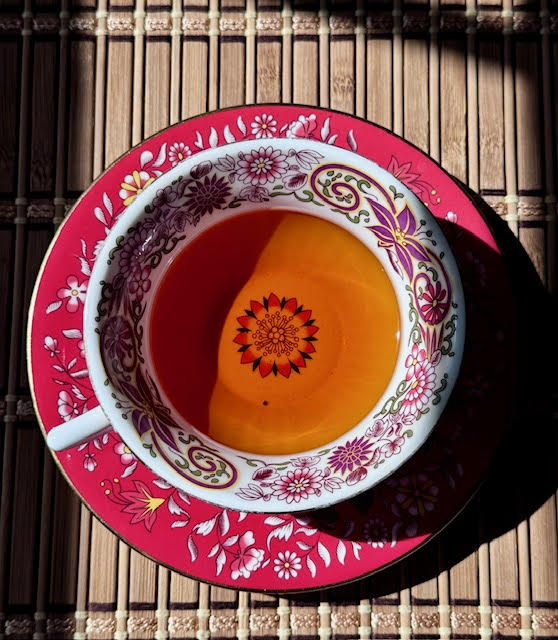 Vibrant, red-orange Bergamot Black tea in a red and white floral Wedgwood teacup and saucer.