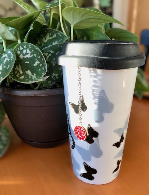 White commuter tea mug with black and gray butterflies. Jeweled tea clip hangs over the side of the mug.