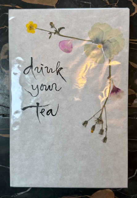 White journal cover with "Drink your tea" in black calligraphy and dried flowers  