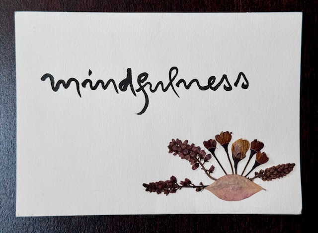 Cream colored card that says "mindfulness" in black calligraphy and includes dried flowers and a leaf. Sold by Blue Cliff Monastery.