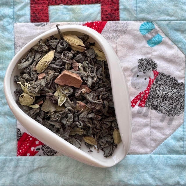 Kashmiri Kahwa--a blend of green tea with cinnamon bark and cardamom--in a white tea scoop on a colorful background with a black sheep wearing a red scarf 