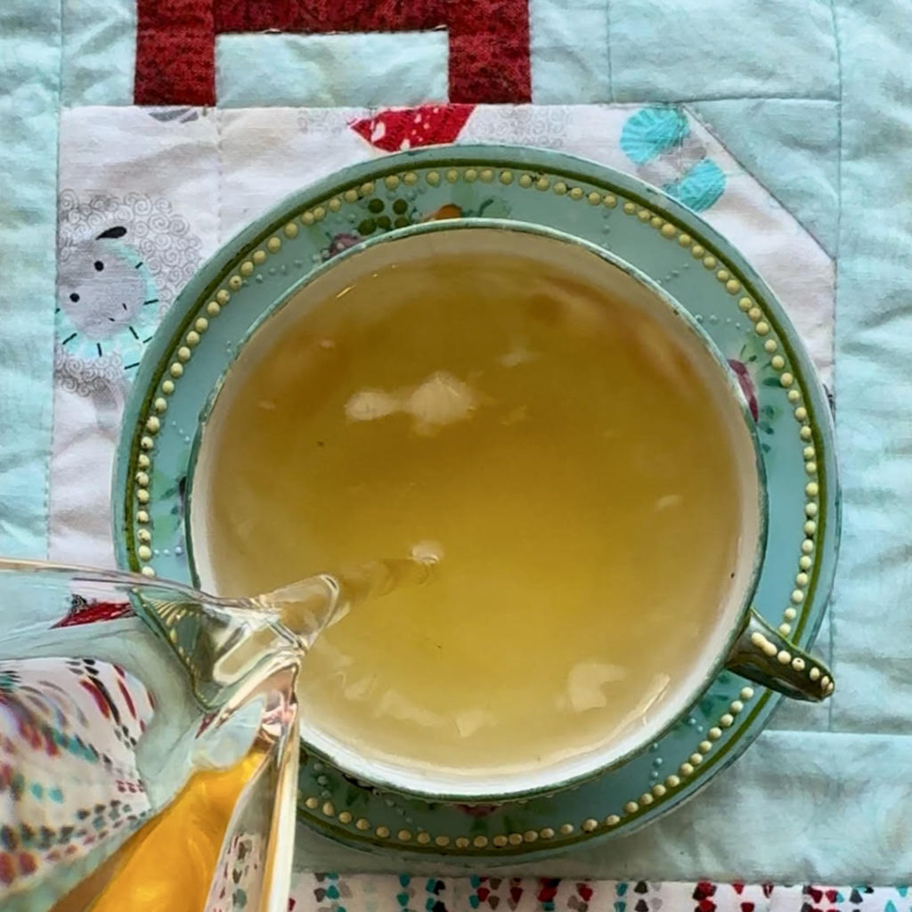 Pouring steeped Kashmiri Kahwa green tea with spices into a blue  teacup with a yellow dot border