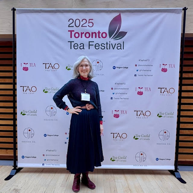 Traci Levy AKA Tea Infusiast standing in front of the 2025 Toronto Tea Festival sign.