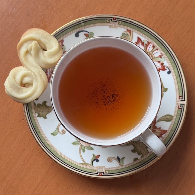 Pairing buttery cookie with tea--pale cookie shaped like a scroll with browned edges rests on the saucer of a teacup filled with Sri Lankan black tea