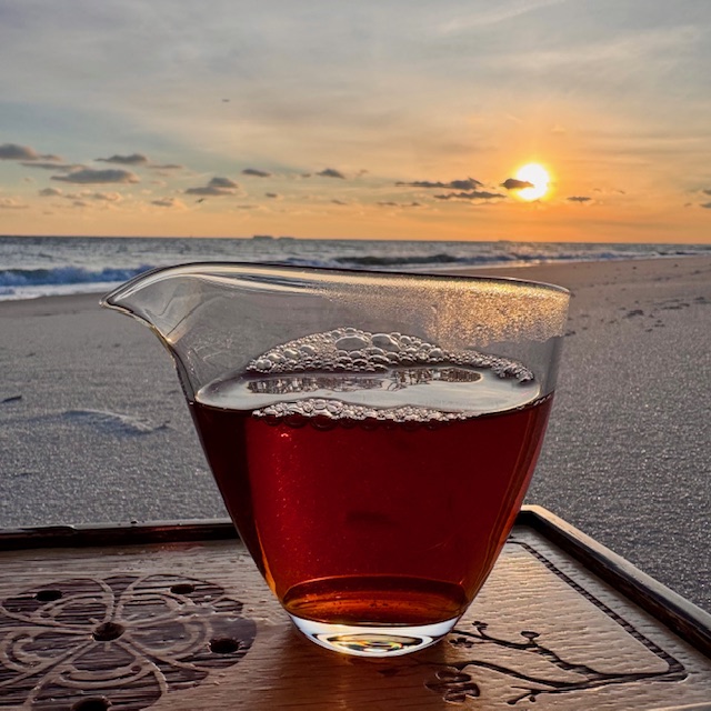 Glass fairness cup, fairness pitcher, or gong dao bei on a wooden tea tray on a beach near sunset