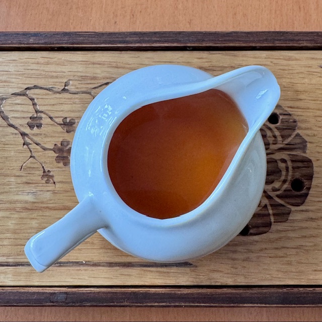 Porcelain fairness cup on a wooden tea tray, full of dark amber tea