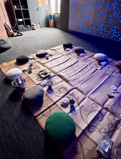 space set up for a tea meditation. It includes meditation cushions, tea bowls, and cloth napkins on a woven mat.